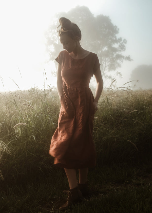 Woman in a dress standing in a field with a soft focus background