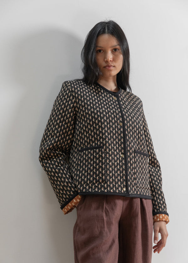 Woman wearing a patterned jacket and brown pants against a plain background