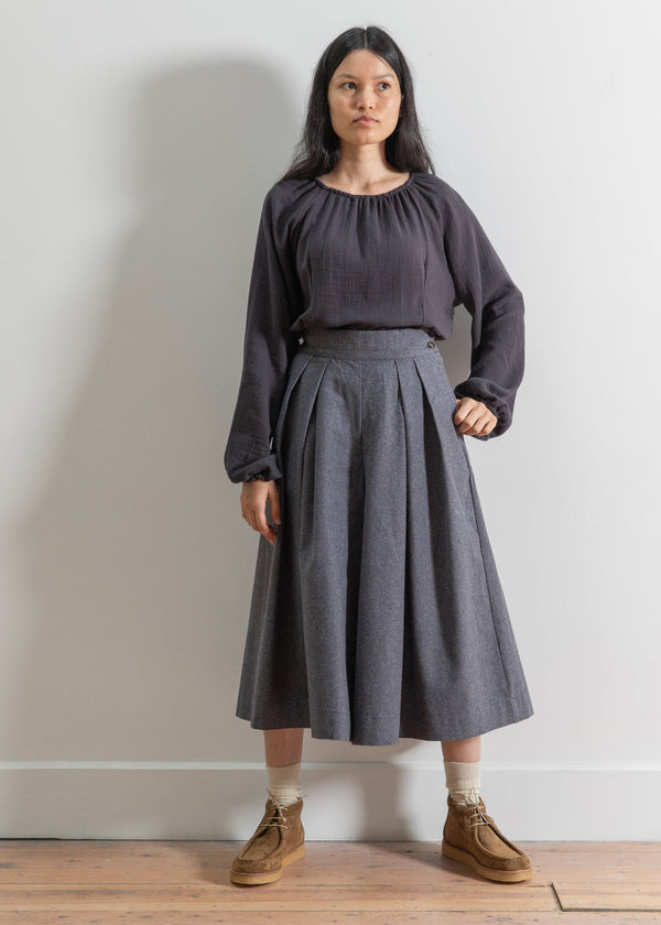 Woman wearing a dark gray outfit with a skirt against a plain background