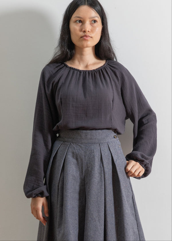 Woman wearing a dark gray blouse and skirt against a plain background