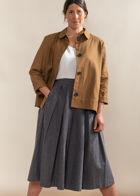 Woman wearing a brown jacket and gray skirt against a beige background