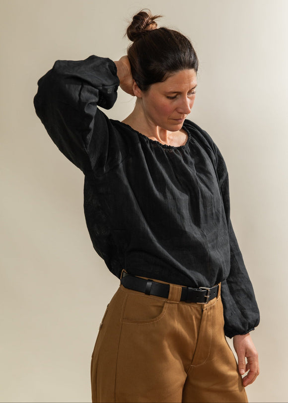 Person wearing a black blouse and brown pants against a plain background