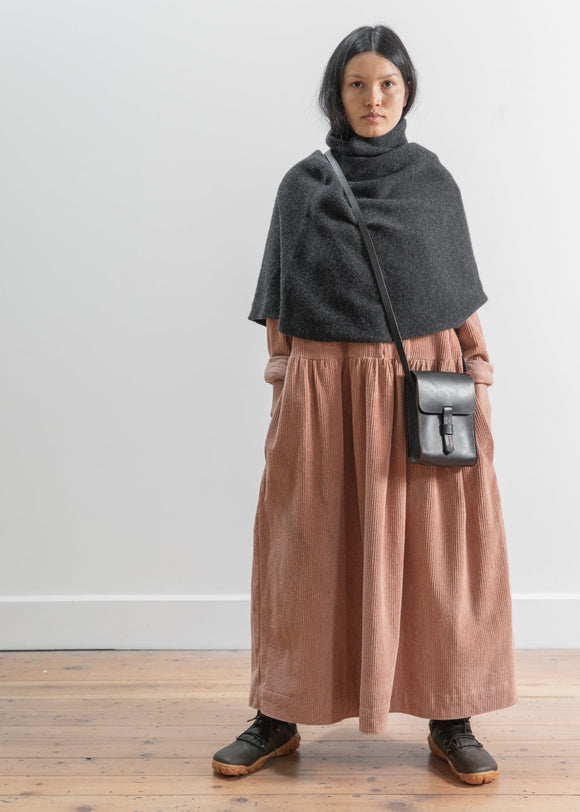 Person wearing a dark gray poncho over a brown dress with a black handbag against a white background
