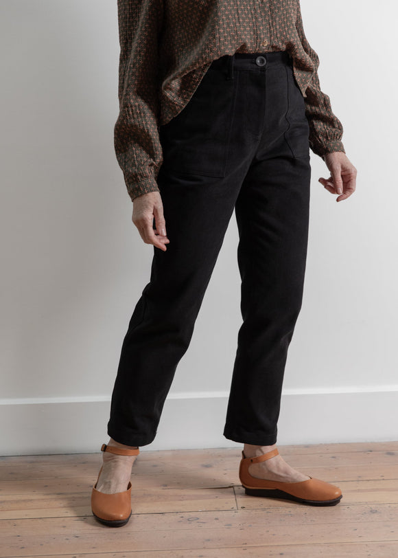 Person wearing black pants and brown shoes on a wooden floor with a white wall background