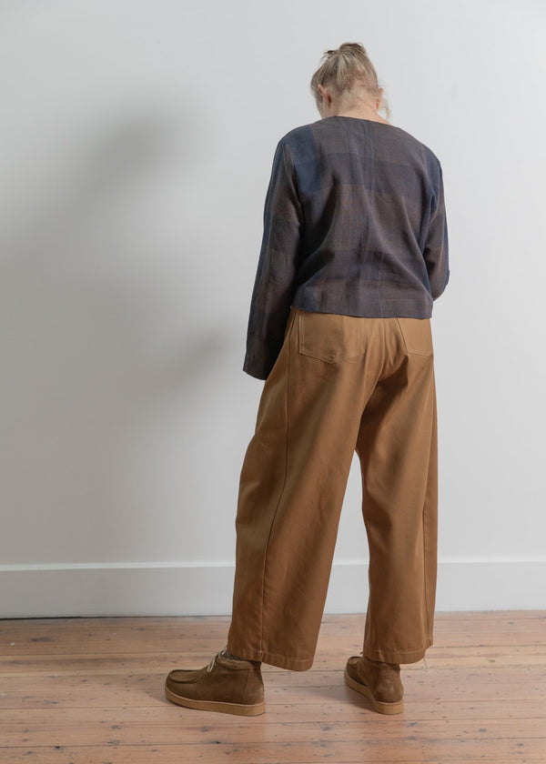 Person wearing a dark sweater and brown pants standing against a white wall.