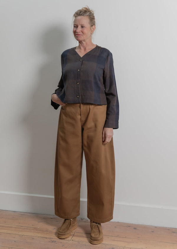 Woman wearing a dark shirt and brown pants standing against a plain wall.
