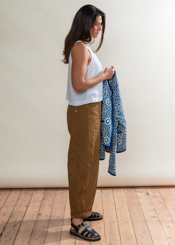 Woman holding a blue patterned jacket against a white wall.