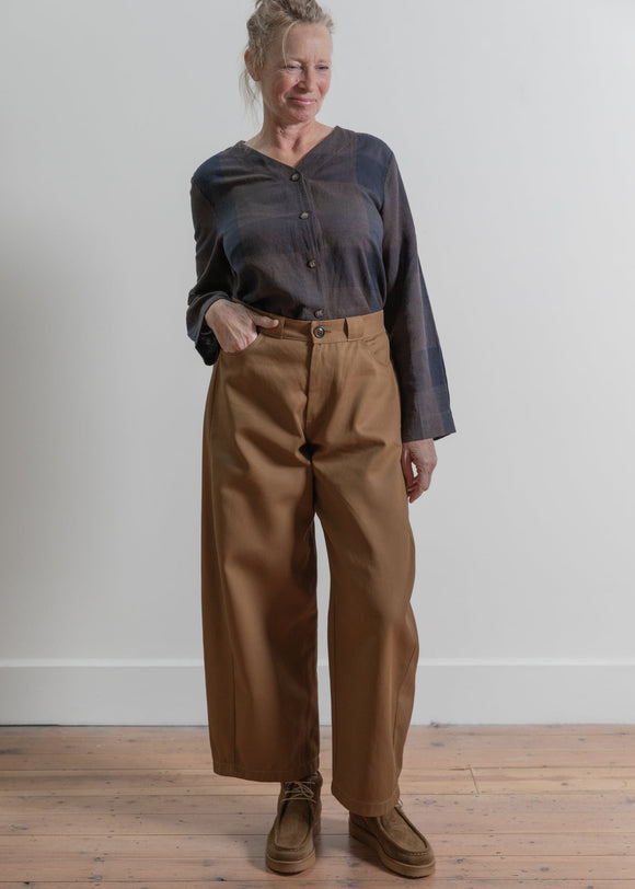Woman wearing a dark shirt and brown pants standing against a plain white wall.