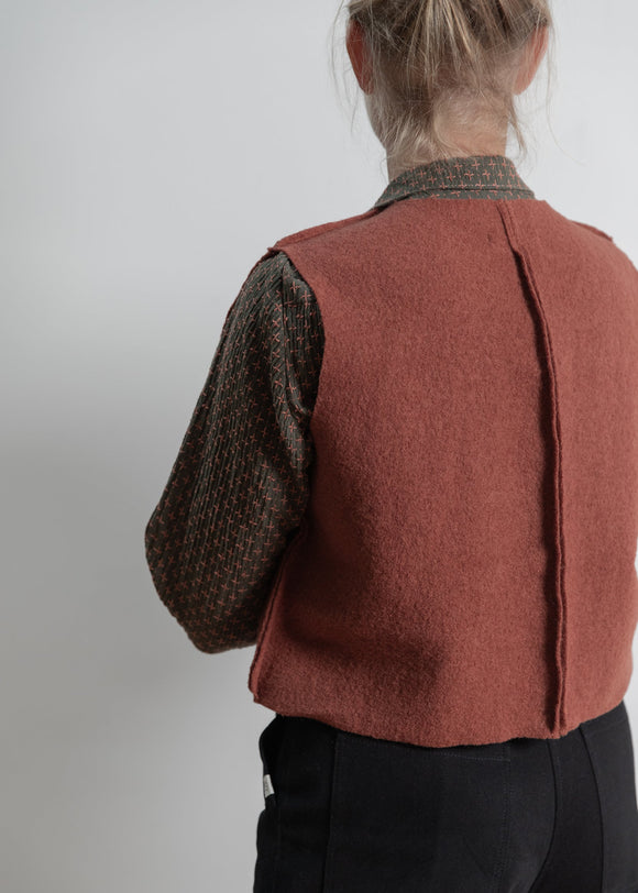 Person wearing a brown vest over a patterned shirt on a plain background