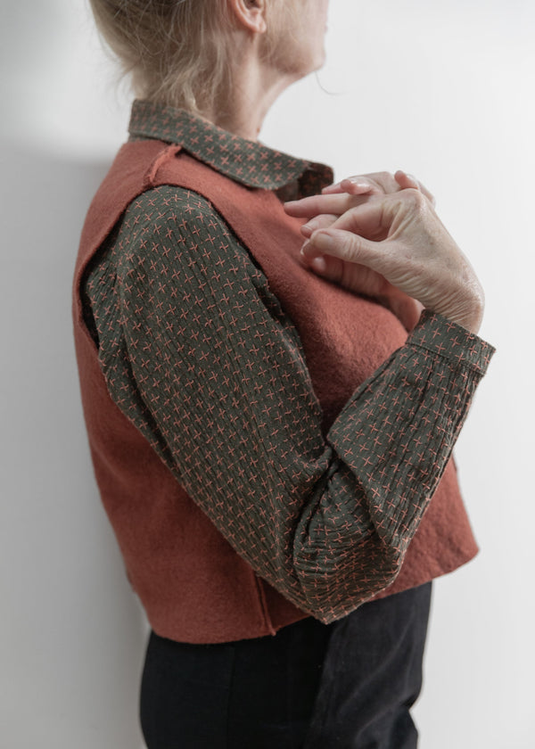 Person wearing a red vest over a patterned shirt against a white background