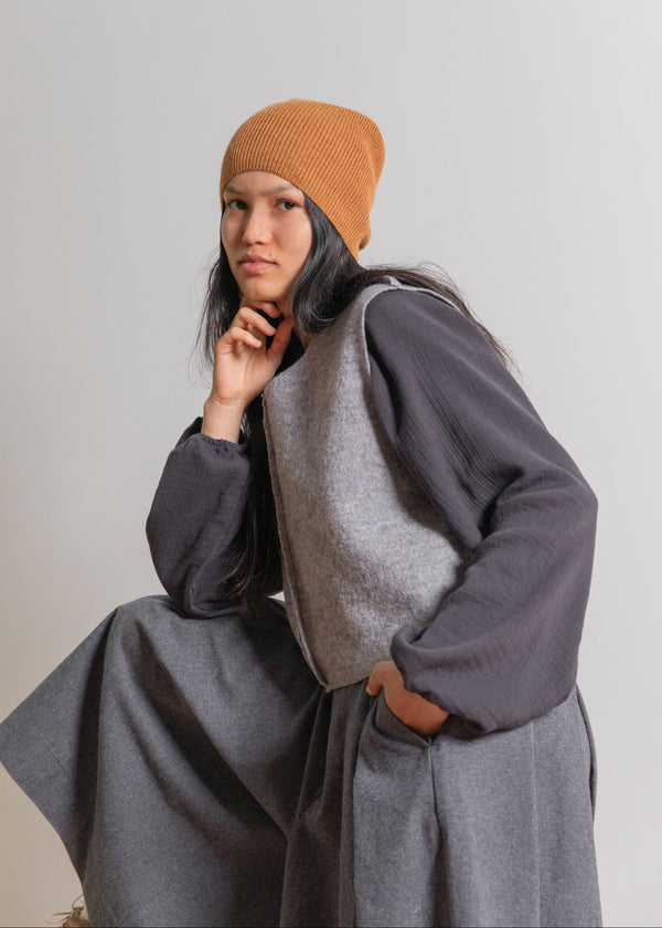 Person wearing a gray coat and brown beanie against a plain background