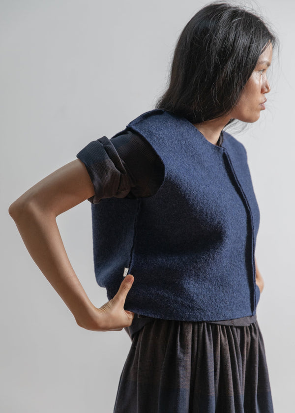 Woman wearing a blue vest over a dark dress against a plain background