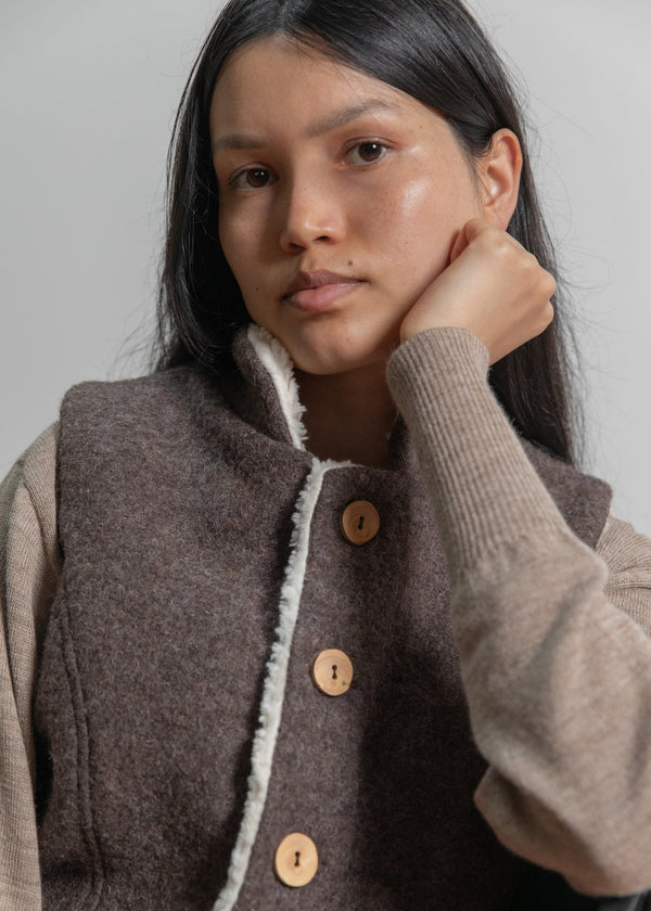 Woman wearing a brown vest with wooden buttons against a plain background
