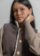 Woman wearing a brown vest with wooden buttons against a plain background