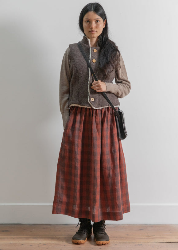Woman wearing a brown checkered skirt and cardigan against a white wall.