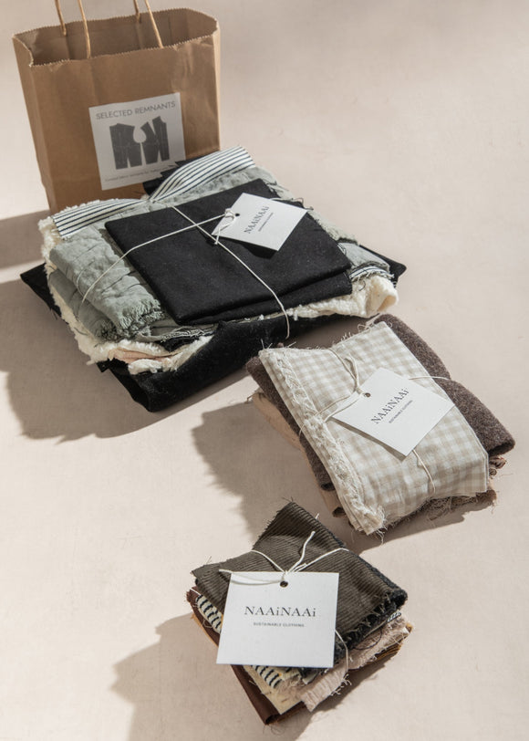 Folded fabric items with tags on a beige surface, next to a brown paper bag.