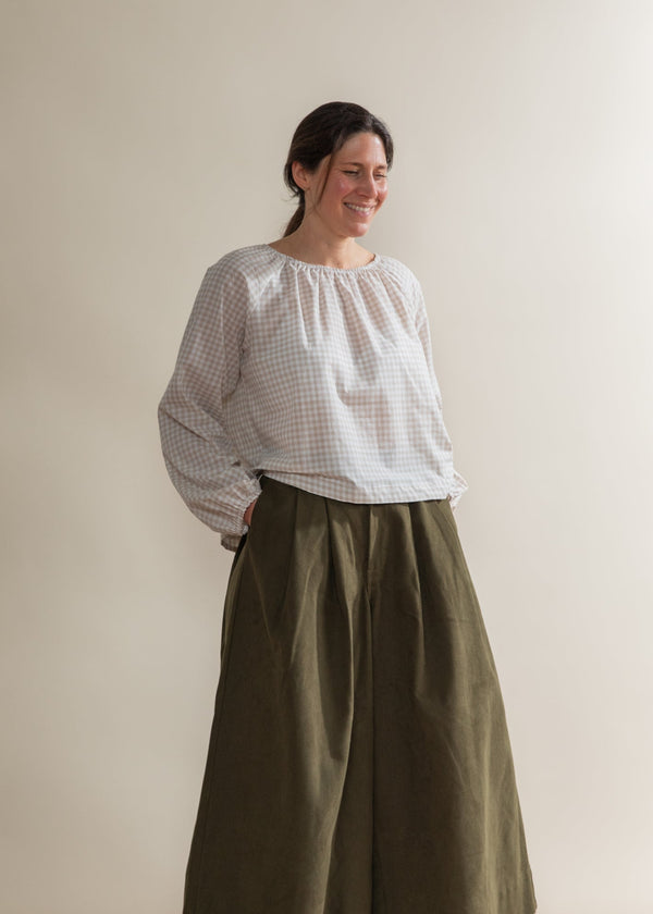 Woman wearing a white blouse and cream skirt against a plain background