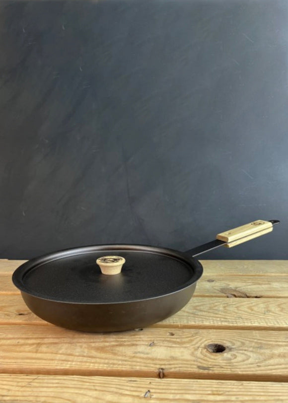 Black frying pan with wooden handle on a wooden surface against a dark background