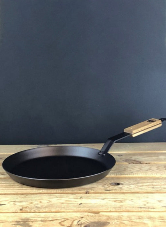 Black frying pan with wooden handle on a wooden surface against a dark background