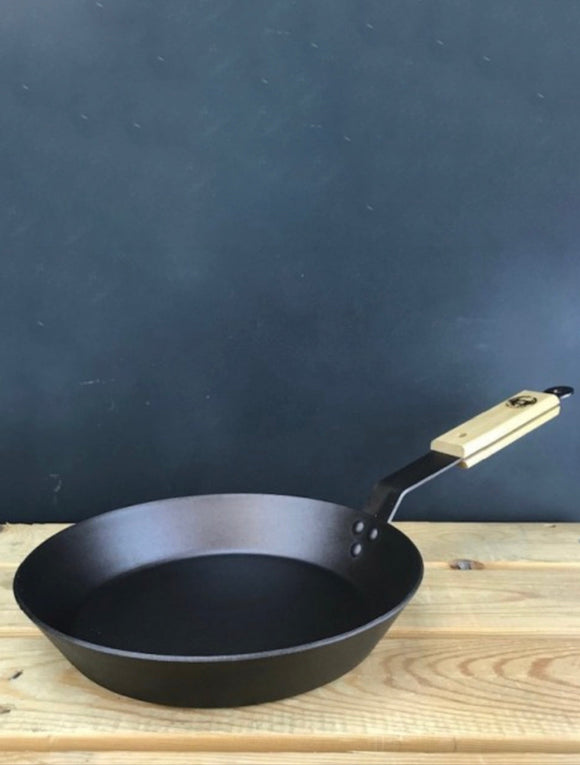 Black frying pan with wooden handle on a wooden surface against a dark blue background