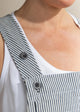 Close-up of a person wearing a white tank top and striped overalls with buttons.