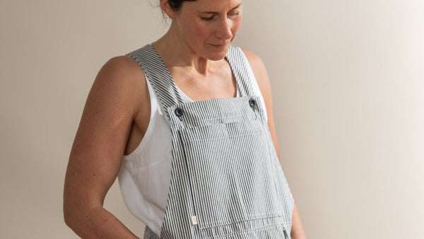 Woman wearing a gray striped overalls against a beige background