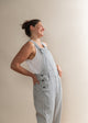 Woman wearing light blue checkered overalls and a white tank top against a plain background