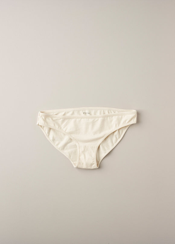 A pair of low waist knickers in a natural beige color, laid flat on a plain background.