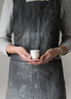 Person wearing a dark apron holding a small white egg cup against a plain background
