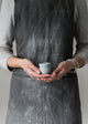 Person wearing a grey apron holding a small white egg cup against a plain background