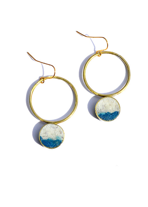 Gold hoop earrings with circular ceramic discs featuring blue and white patterns on a white background