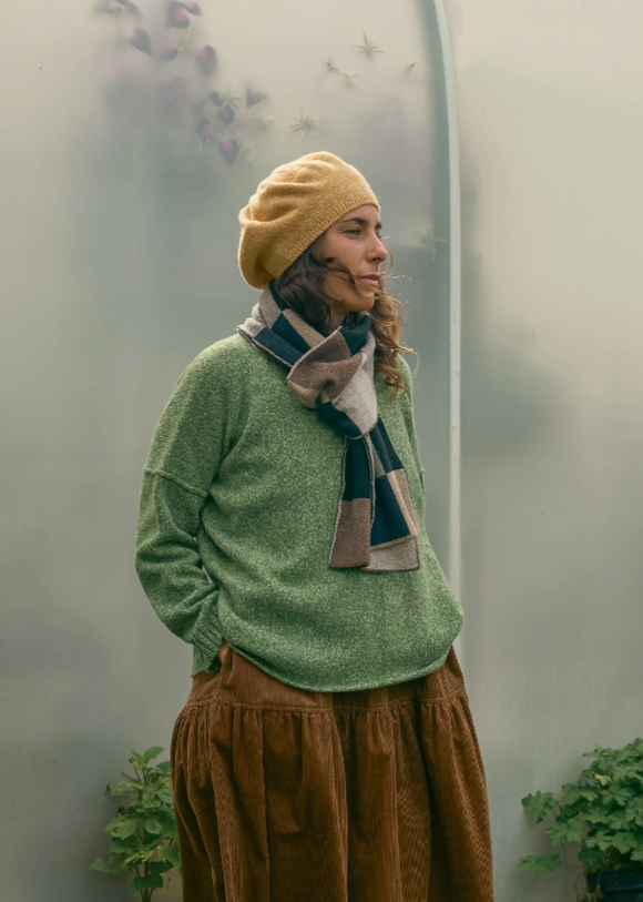 A person wearing a chequerboard scarf in a garden, the scarf is predominantly in shades of brown, navy, black, grey, nutmeg, and oatmeal.