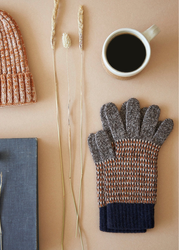 Knitted hat, gloves, book, and cup of coffee on a beige surface