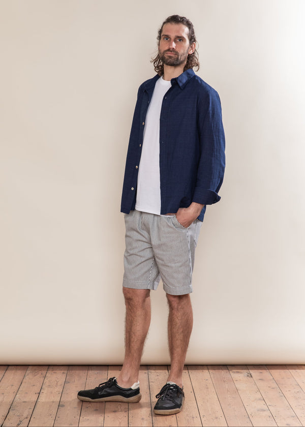 Man wearing a navy shirt over a white t-shirt with gray shorts against a plain background