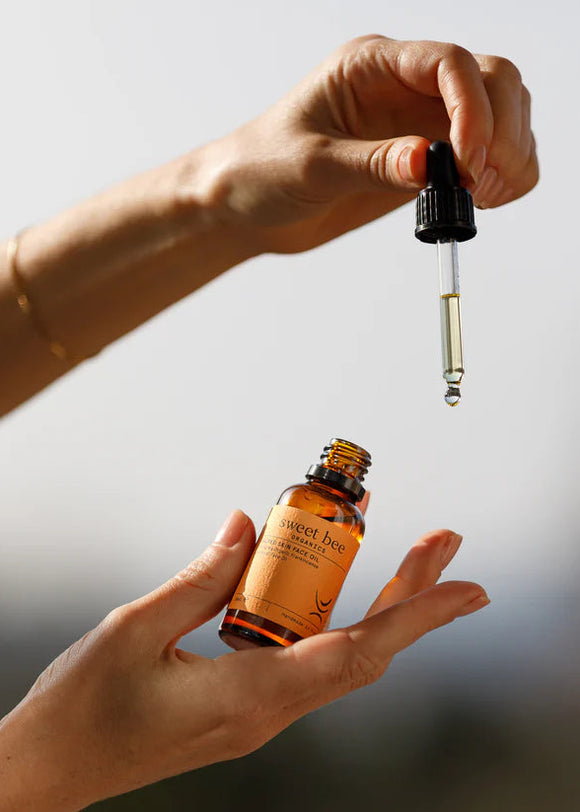 Hand holding a bottle of sweet hog balm with a dropper, against a neutral background