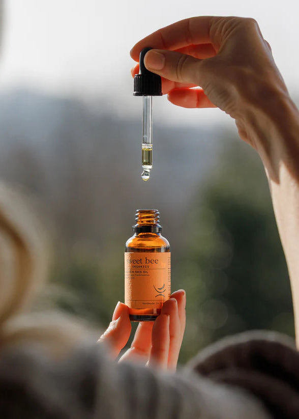 Person holding a bottle of 'Sweet Bee' product with a dropper, blurred natural background
