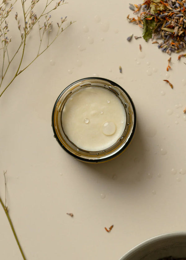Jar of cream on a light surface with dried herbs and flowers