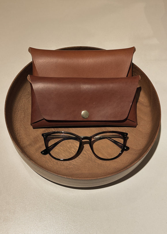 Brown leather case with a button and black glasses on a beige surface