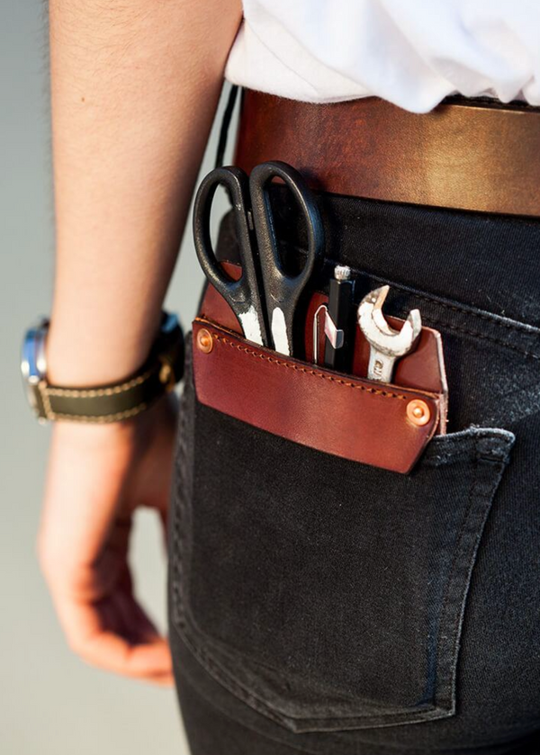 Person wearing a leather tool pouch with tools on a plain background