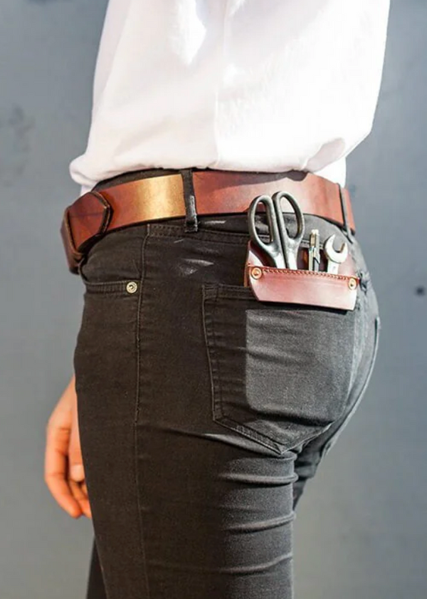 Person wearing a white shirt and dark pants with a brown belt and gun holster on a beach.
