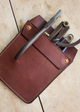 Brown leather multi-tool pouch with tools on a beige surface