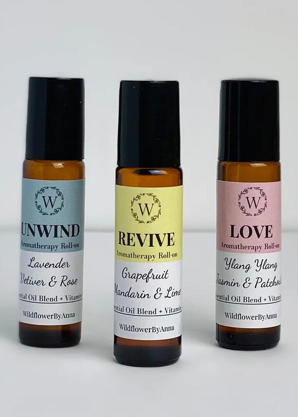 Three aromatherapy roll-on bottles with labels UNWIND, REVIVE, and LOVE, each with a different color cap and label text indicating the scents used.