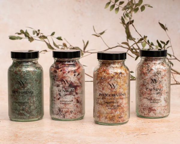 Four jars of bath salts with labels on a wooden surface with a plant in the background