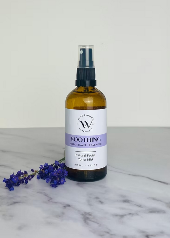 A bottle of facial toner mist labeled 'SOOTHING' with a spray nozzle, surrounded by a few sprigs of dried lavender on a marble surface.