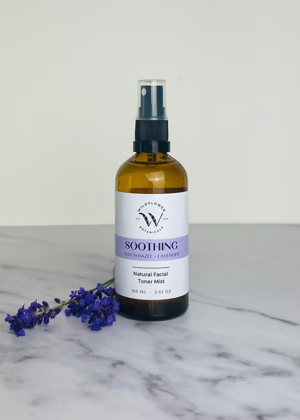A bottle of facial toner mist labeled 'SOOTHING' with a spray nozzle, surrounded by a few sprigs of dried lavender on a marble surface.