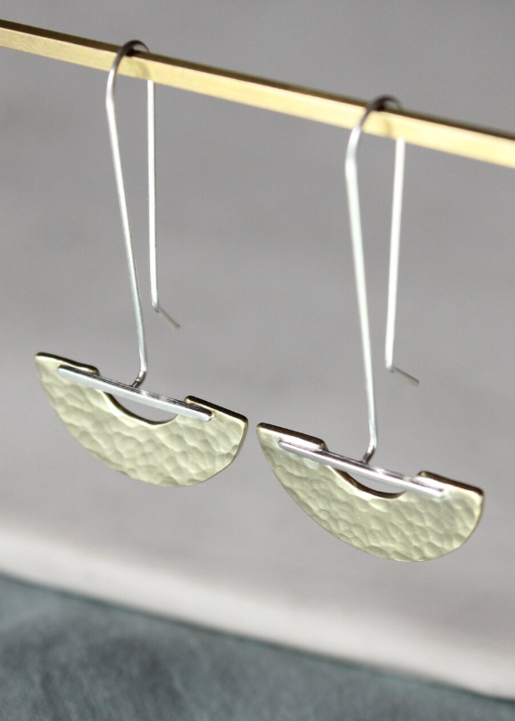 Silver earrings with textured design hanging on a rod against a neutral background