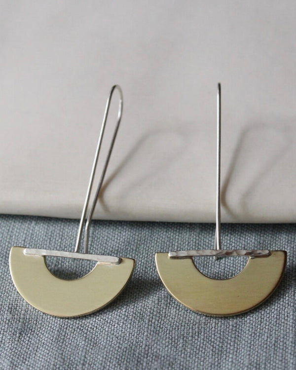 Silver earrings with half-circle designs on a gray surface