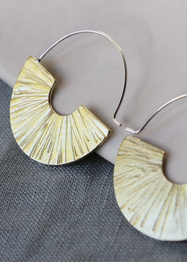 A pair of silver-colored hoop earrings with a textured surface, displayed on a grey background.