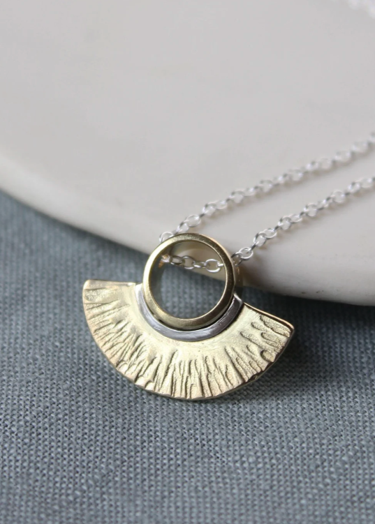 A silver and brass textured Eos pendant with a striped design, displayed on a white surface.