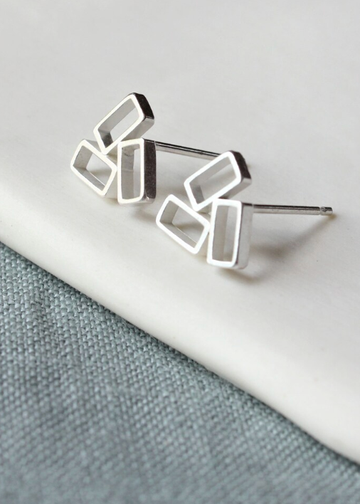 A pair of silver geometric stud earrings placed on a white surface with a grey background.